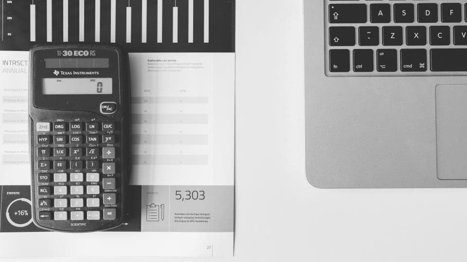 A calculator on a printed bar-chart report beside a laptop keyboard, in black and white.